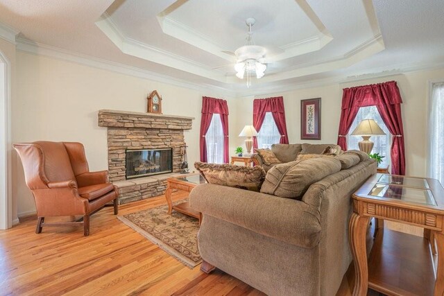 living room with light wood-type flooring, a tray ceiling, ceiling fan, crown molding, and a fireplace