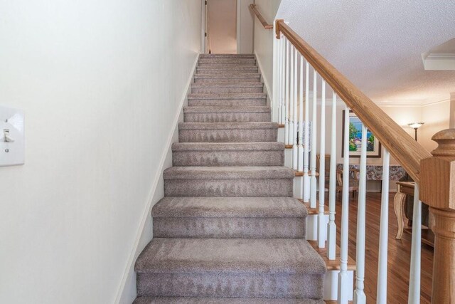 stairs with crown molding, hardwood / wood-style floors, and a textured ceiling