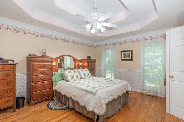 bedroom featuring light hardwood / wood-style floors, a raised ceiling, multiple windows, and ceiling fan