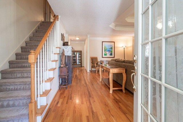 entryway featuring light hardwood / wood-style floors, ornamental molding, a textured ceiling, and a tray ceiling