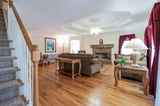 living room with a raised ceiling, a fireplace, wood-type flooring, and ornamental molding