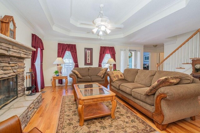 living room with light hardwood / wood-style floors, a raised ceiling, ornamental molding, and a wealth of natural light