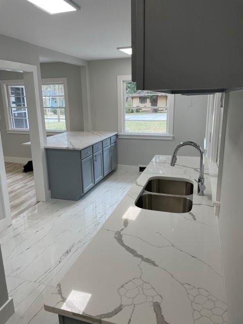 kitchen with light stone countertops, marble finish floor, and a sink