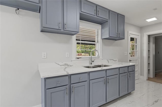 kitchen featuring marble finish floor, gray cabinetry, light stone countertops, and a sink