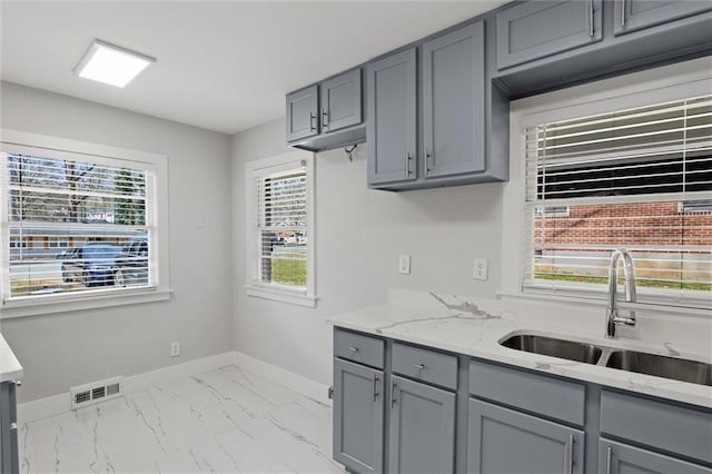 kitchen featuring visible vents, marble finish floor, gray cabinetry, a sink, and baseboards