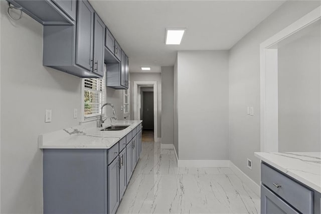 kitchen featuring light stone counters, baseboards, gray cabinets, a sink, and marble finish floor