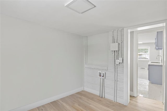 empty room with light wood-style flooring, baseboards, and a sink