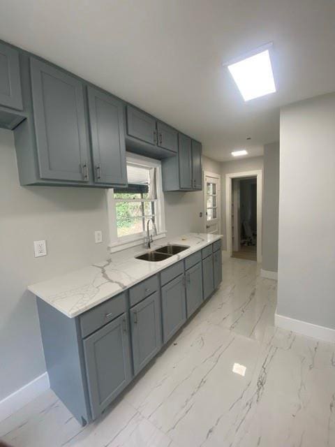 kitchen with gray cabinetry, baseboards, marble finish floor, and a sink