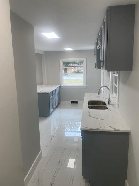 kitchen with visible vents, baseboards, gray cabinets, marble finish floor, and a sink