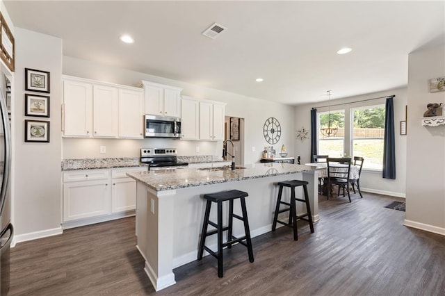 kitchen featuring white cabinets, appliances with stainless steel finishes, dark hardwood / wood-style floors, and an island with sink