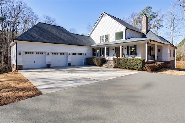 view of front of home with roof with shingles, a chimney, covered porch, an attached garage, and driveway