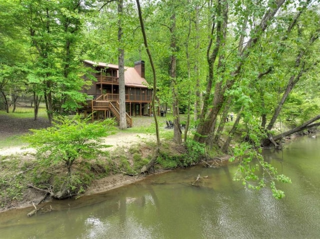 rear view of property featuring stairway, a deck, a chimney, and a view of trees