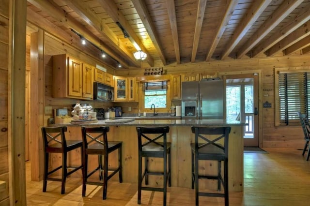 kitchen with beam ceiling, wooden walls, black microwave, stainless steel fridge with ice dispenser, and light wood-style floors