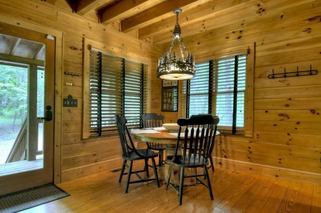 dining room with wood walls, wood finished floors, beamed ceiling, and a notable chandelier