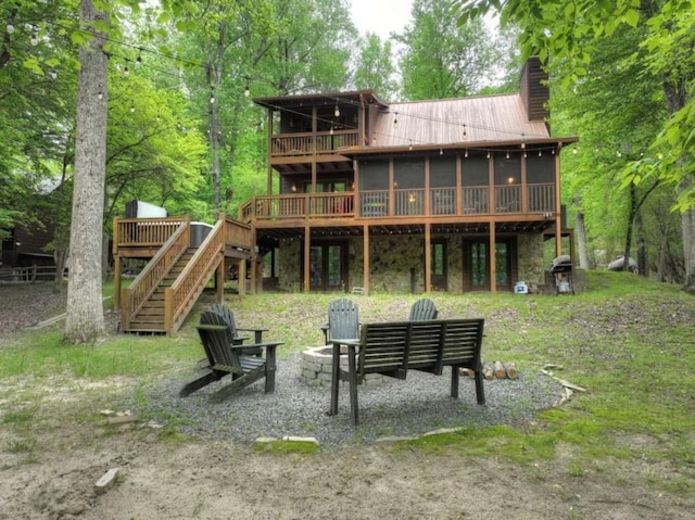 rear view of property featuring a sunroom, a fire pit, a deck, metal roof, and stairs