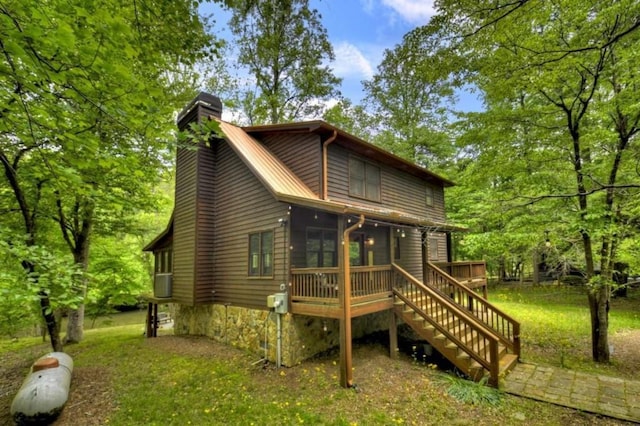 back of property with a sunroom, a chimney, a wooden deck, a yard, and stairs