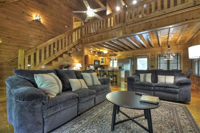 living area featuring wood ceiling, ceiling fan with notable chandelier, stairs, wooden walls, and light wood-type flooring