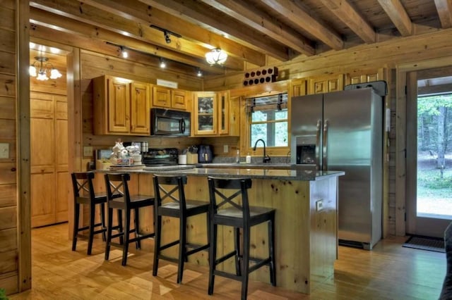 kitchen with beam ceiling, black microwave, stainless steel fridge with ice dispenser, wooden walls, and light wood-type flooring