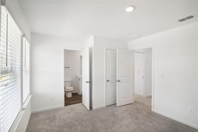 unfurnished bedroom featuring ensuite bath and light colored carpet