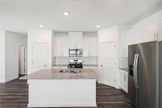 kitchen featuring white cabinetry, appliances with stainless steel finishes, light stone countertops, and a center island with sink