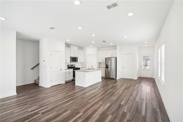 kitchen with white cabinetry, stainless steel appliances, dark hardwood / wood-style floors, light stone countertops, and a center island with sink