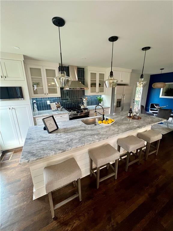 kitchen with sink, hanging light fixtures, stainless steel appliances, wall chimney range hood, and white cabinets