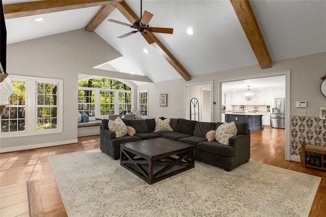 living area with beamed ceiling, a ceiling fan, high vaulted ceiling, wood finished floors, and a chandelier