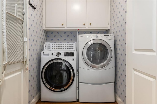 washroom featuring washing machine and clothes dryer, wallpapered walls, cabinet space, and baseboards