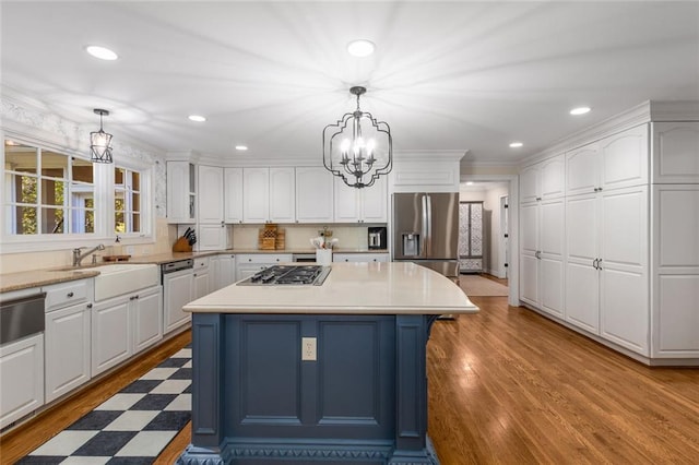 kitchen with stainless steel appliances, white cabinetry, wood finished floors, a chandelier, and a sink