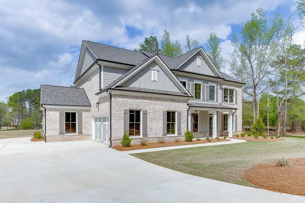 view of front facade featuring driveway, a front yard, roof with shingles, board and batten siding, and brick siding