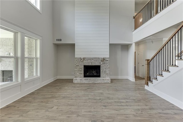 unfurnished living room with a brick fireplace, light wood-type flooring, and a towering ceiling