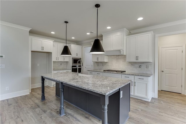 kitchen with appliances with stainless steel finishes, hanging light fixtures, an island with sink, white cabinets, and wall chimney range hood