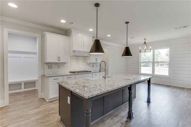 kitchen with light stone countertops, white cabinetry, a kitchen island with sink, and hanging light fixtures