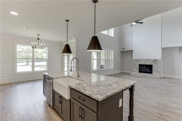 kitchen featuring a brick fireplace, light hardwood / wood-style floors, sink, dishwasher, and pendant lighting