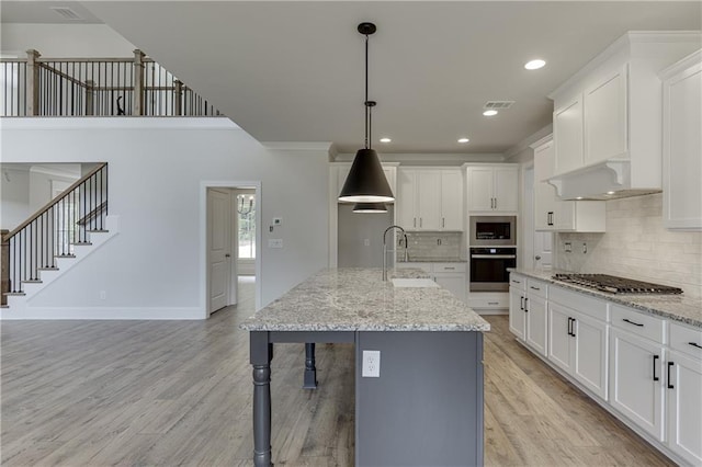 kitchen featuring white cabinets, a center island with sink, stainless steel appliances, and decorative light fixtures