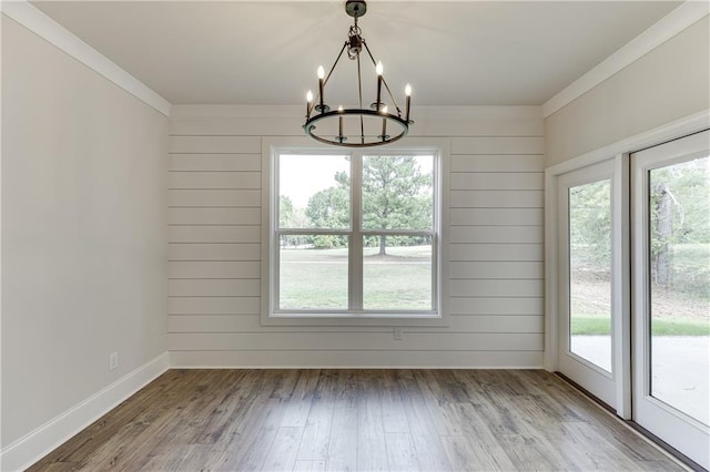 unfurnished dining area with a chandelier, crown molding, and wood-type flooring