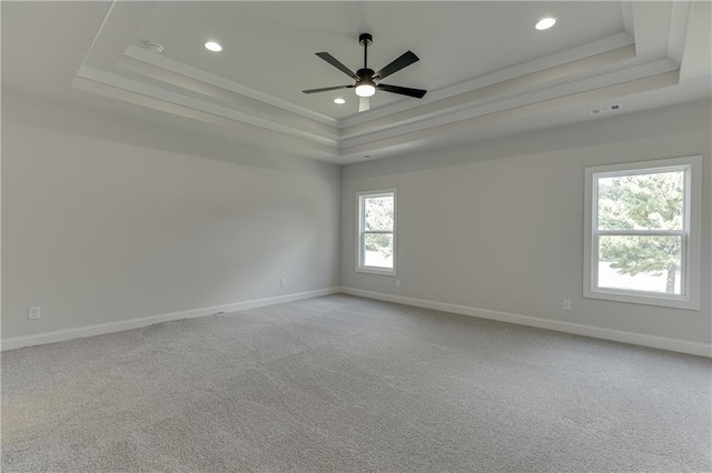 carpeted empty room with a raised ceiling, ceiling fan, and ornamental molding