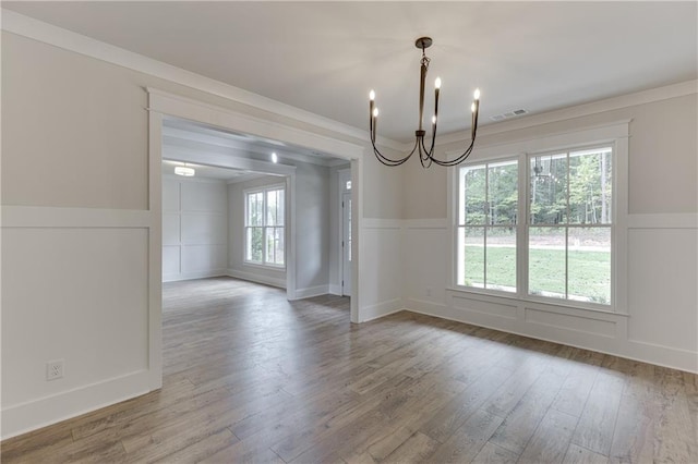 unfurnished dining area with hardwood / wood-style flooring, crown molding, and a notable chandelier