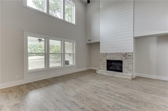 unfurnished living room featuring a brick fireplace, light hardwood / wood-style flooring, and a towering ceiling