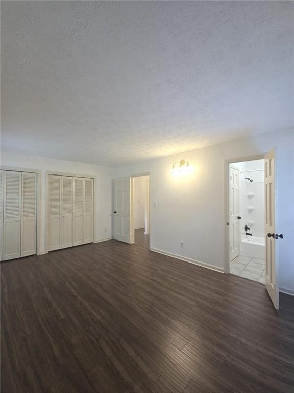 2821 NE Meadowlark Trl, Duluth, GA 30096 - unfurnished bedroom with dark wood-type flooring, baseboards, two closets, ensuite bath, and a textured ceiling