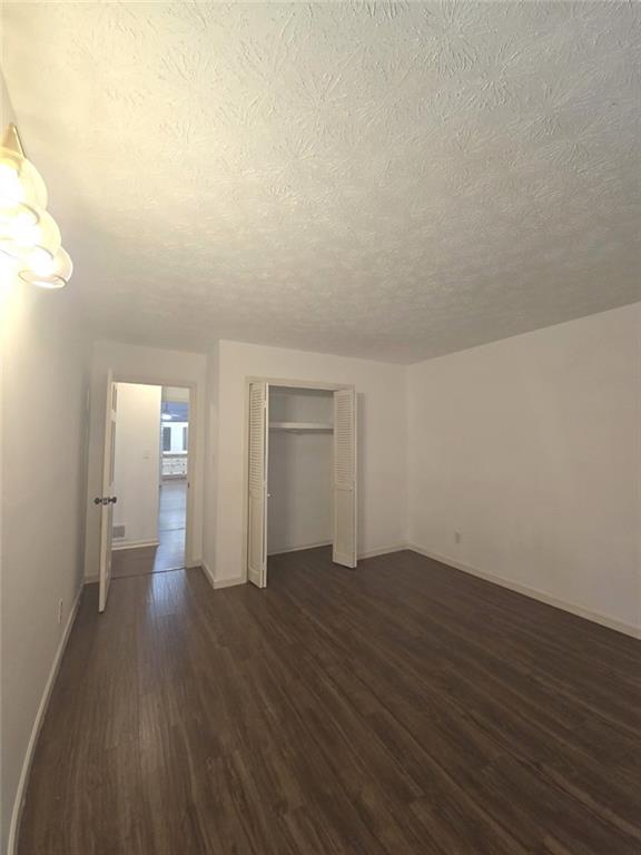 2821 NE Meadowlark Trl, Duluth, GA 30096 - unfurnished bedroom featuring dark wood-style flooring, a textured ceiling, baseboards, and a closet