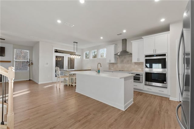 kitchen featuring light countertops, stainless steel appliances, white cabinetry, backsplash, and wall chimney range hood