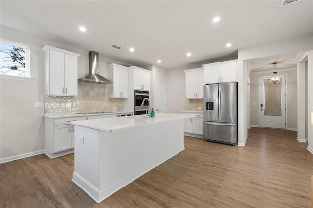 kitchen featuring tasteful backsplash, wall chimney exhaust hood, light wood finished floors, light countertops, and appliances with stainless steel finishes