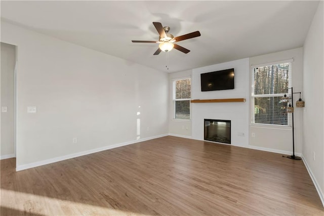 unfurnished living room featuring baseboards, a glass covered fireplace, ceiling fan, and wood finished floors