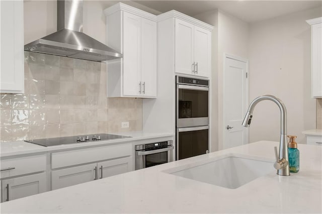 kitchen with double oven, a sink, wall chimney range hood, black electric stovetop, and tasteful backsplash