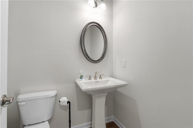 half bath featuring baseboards and toilet