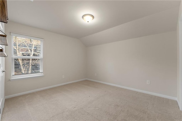 carpeted spare room with vaulted ceiling and baseboards