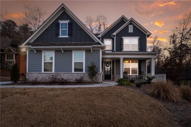 craftsman-style home featuring a porch, a front yard, stone siding, and board and batten siding
