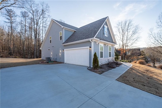 view of side of property with central air condition unit, a shingled roof, driveway, and stone siding