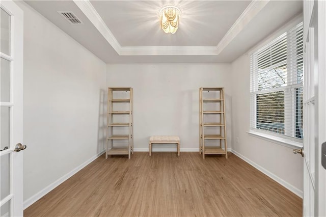 spare room with ornamental molding, visible vents, light wood finished floors, a raised ceiling, and baseboards